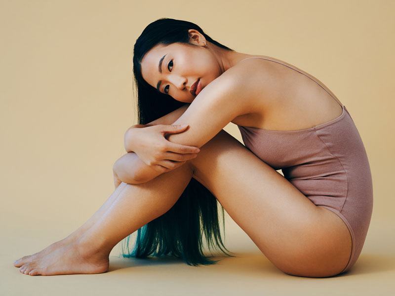 woman with flawless skin sitting on studio floor and hugging her knees